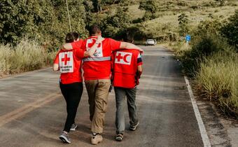 Three Brazilian Red Cross volunteers hug as they walk together in Jucurucu, Bahia State in January 2022 where they are delivering food packages and providing psychosocial support to local communities.