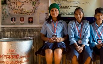 Three female junior Red Cross volunteers in Nepal sit together in their secondary school in Madi, Chitawan province, where they have been trained in how to prepare for earthquakes and other disasters and share this knowledge with their communities.