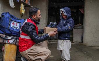 An Afghan Red Crescent volunteer gives a small boy in Paktika province, Afghanistan a new pair of warm winter shoes in January 2023 to help him stay warm during the harsh winter. The Afghan Red Crescent, supported by the IFRC, is providing communities in the region with winter kits to help them cope.