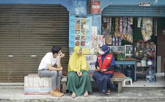 An Indonesian Red Cross volunteer sits with two people outside their shop in Banten province and hears how the COVID-19 pandemic affected them and their business, and how cash assistance provided by the Indonesian Red Cross helped them to get by.