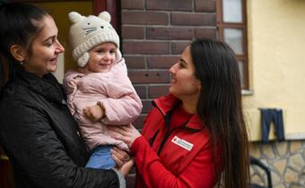 A mother from Ukraine, Alissa, holds her young daughter and speaks to Hungarian Red Cross volunteer, Kateryna, about her life since fleeing international armed conflict in Ukraine in 2022.