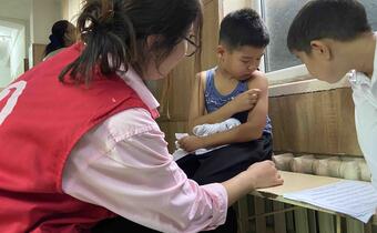 A Kyrgyzstan Red Crescent volunteer administers a measles vaccine to a young boy.