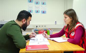 A volunteer with the Slovenian Red Cross offers a Slovenian language lesson to a man who recently migrated to the country.
