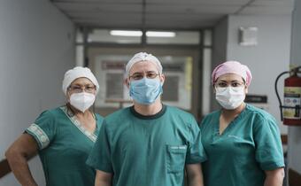 Three members of the Reina Sofía Hospital healthcare staff pose in a hallway, smiling through their medical masks and uniforms.