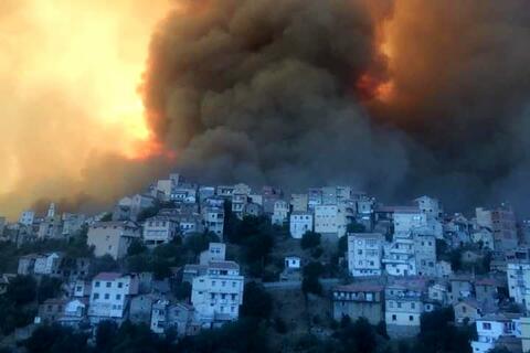 قرية في الجزائر تلفها سحابة من الدخان الناجم عن حرائق الغابات في أوائل أغسطس /آب 2021، والتي هددت حياة الآلاف وألحقت الضرر بالنظم البيئية المحلية والبنية التحتية وسبل العيش.