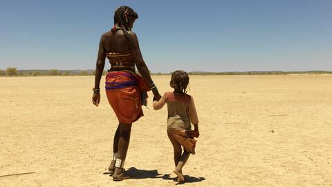 Mbeungua, de 47 años, y su hija de 6 años caminan hacia la aldea de Oukongo, en Namibia, donde muchos refugiados angoleños se han reubicado debido a la dura sequía que afecta a su país.