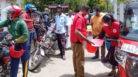 Des volontaires de la Croix-Rouge sri-lankaise distribuent des boissons gazeuses et des en-cas aux personnes faisant la queue dans les stations-service, fin mai 2022.