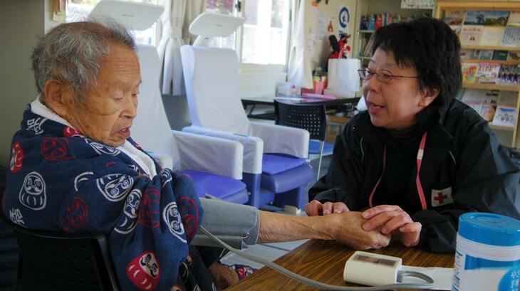 Un membre de la Croix-Rouge japonaise vérifie la tension artérielle d'un résident âgé dans une cité de logements préfabriqués, dans le cadre d'activités régulières de soutien et de rencontres sociales.
