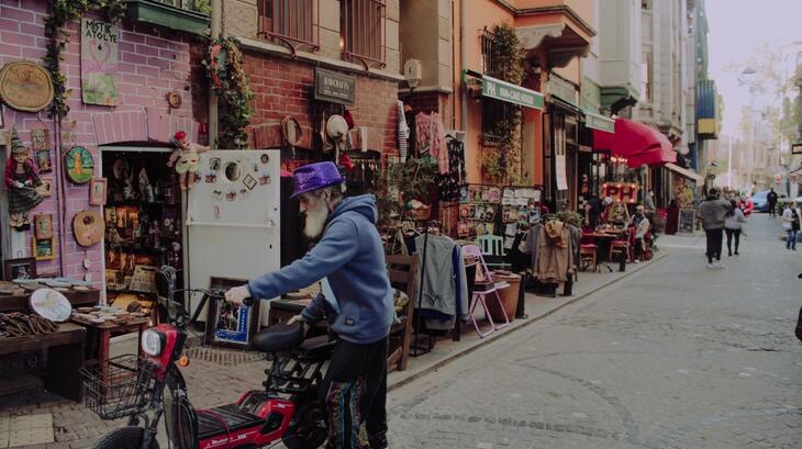 A shot of a man standing with his bike outside an antique shop in Balat neighbourhood, Istanbul by ESSN Storyteller, Luai. Luai says "I found this man wearing this dress and realized that he is a Jew. He still lives in the same neighborhood, and he is the owner of the antique shop in the picture. I was very impressed by the photo because it contains many stories and combines modernity, history, and religious coexistence in this neighborhood."