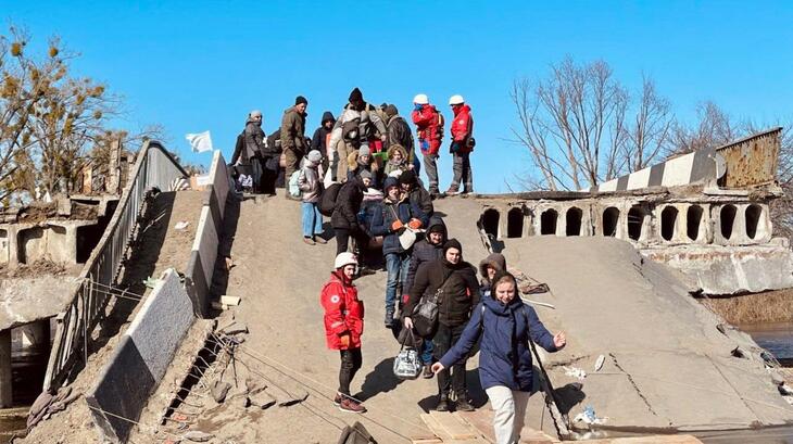 Ukrainian Red Cross volunteers assist thousands of people to cross a temporary bridge they constructed in Demydiv, Ukraine to help people flee conflict, after the original bridge was blown up in February 2022.