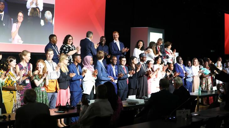 Jóvenes voluntarios y voluntarias se reúnen en el escenario como parte de una inspiradora ceremonia de apertura de la Asamblea General de 2022. Los voluntarios llevaron a los delegados a un viaje humanitario en siete capítulos hacia el pasado, el presente y el futuro.