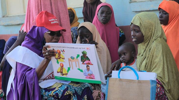 In Katsina state, Nigeria, a Nigerian Red Cross volunteer speaks to nursing mothers in August 2022 about how they can keep their children healthy and well-nourished as part of their Mother's Club initiative to help families cope with the ongoing hunger crisis.