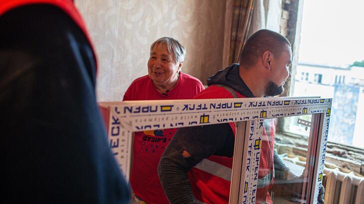 A woman in Vinnytsia, Ukraine, smiles as Ukrainian Red Cross volunteers repair windows in his house that had been damaged by rocket strikes in July 2022. The new windows will help him and his family stay warm throughout the cold winter months.