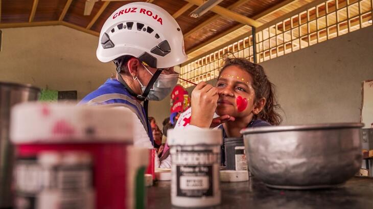 Un volontaire de la Croix-Rouge vénézuélienne peint le visage d'une jeune fille de Las Tejerias dont la famille a été touchée par les fortes pluies et les inondations qui frappent le pays depuis septembre 2022. En plus de fournir des abris, des secours d'urgence et des services de santé, les volontaires apportent un soutien psychosocial et de santé mentale aux enfants et aux adultes pour les aider à faire face à la situation.