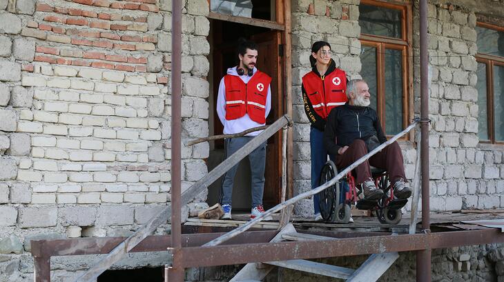 Deux volontaires de la Croix-Rouge de Géorgie aident un homme en fauteuil roulant à prendre l'air sur un balcon. En avril 2023, des volontaires ont distribué des colis alimentaires et fourni une assistance médicale à de nombreuses personnes vulnérables dans des communautés à travers le pays.