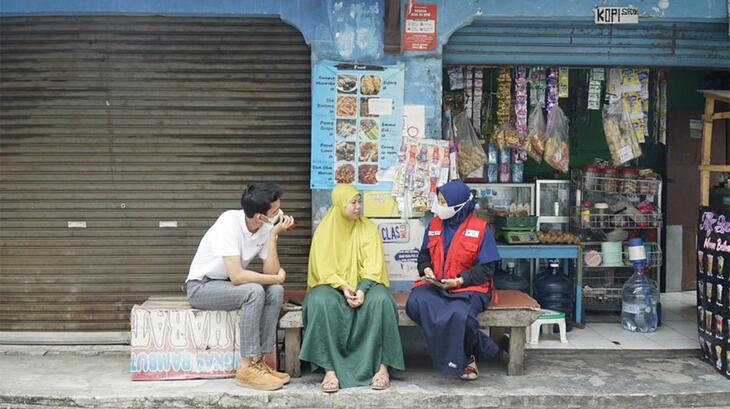 An Indonesian Red Cross volunteer sits with two peopleمتطوعة في الصليب الأحمر الإندونيسي تجلس الى جانب شخصين خارج متجرهما في مقاطعة بانتين، وتستمع الى كيف أثرت عليهما جائحة كوفيد-19، وكيف ساعدتهما المساعدات النقدية التي قدمها الصليب الأحمر الإندونيسي. 