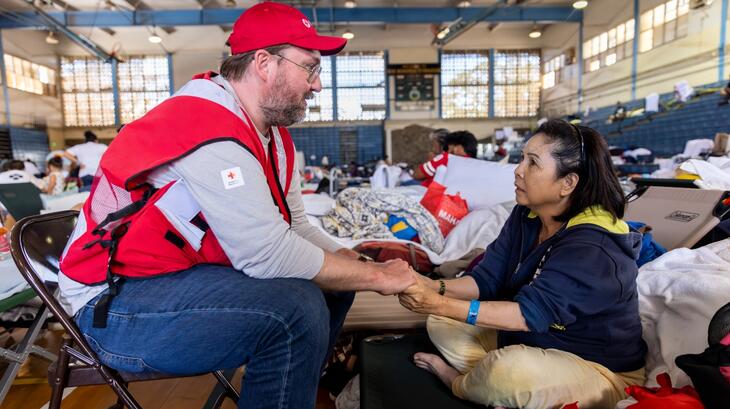 An American Red Cross worker holds hands with and comforts a woman in a Red Cross shelter in Maui following devastating wildfires in August 2023 that swept through Lahaina town.