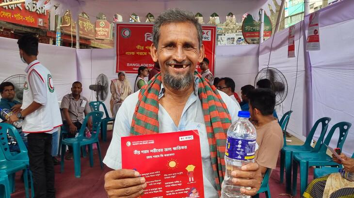 A rickshaw driver in Dhaka, Bangladesh smiles after getting some water and some relief from extreme heat at a cooling station set up by the Bangladesh Red Crescent Society during a long-lasting heatwave in May 2024.