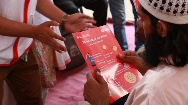 A man at a Bangladesh Red Crescent cooling station reads an information pamphlet on how to stay safe during extreme heat waves.
